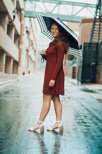 Full length of young woman standing in rain on road