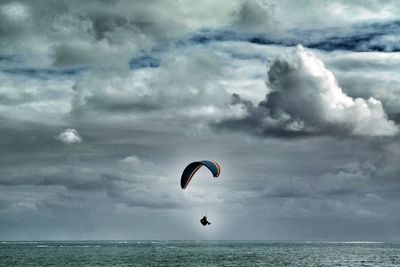 Person paragliding over sea against sky