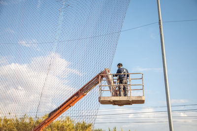 Low angle view of man working on fence