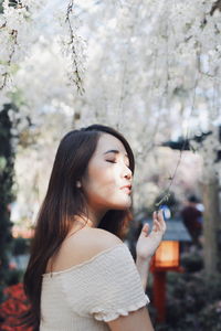 Young woman looking away while standing against trees