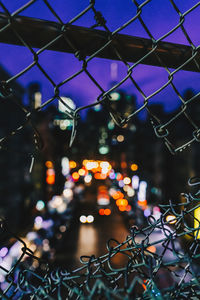 Illuminated lights seen through damaged chainlink fence at night