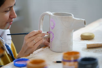 Artist woman hold paintbrush creating ornament on clay jug in pottery studio. ceramist workplace
