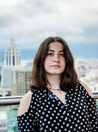 Portrait of beautiful woman standing against cloudy sky in city