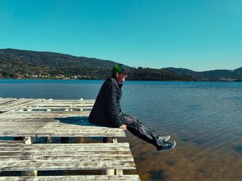 Side view of young man against lake against clear blue sky