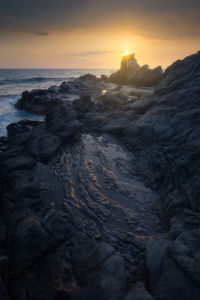 Rocks on sea shore against sky during sunset