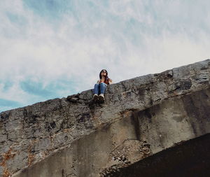 Low angle view of woman sitting on bridge against sky