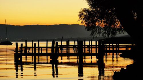 Silhouette wooden posts in lake against sky during sunrise