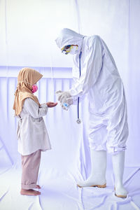 Full length of man wearing protective suit giving hand sanitizer against white background