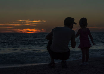 Rear view of friends standing on beach against sky during sunset