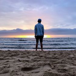 Rear view of silhouette man standing on beach against sky