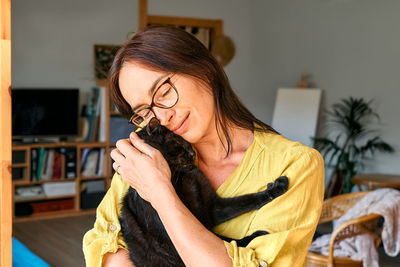 Middle-aged woman hugging cute black cat in indoor scene. human-animal relationships. funny home pet