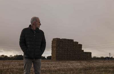 Adult man in winter clothes in fields with group of straw bales