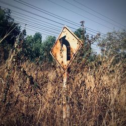 Low angle view of rusty sign on field against sky