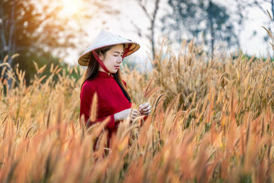 Woman in asian style conical hat standing amidst plants