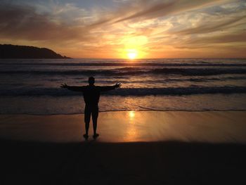Silhouette man standing at beach against sky during sunset