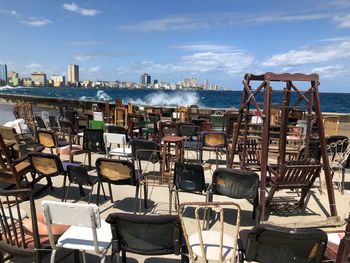 Empty chairs and tables by sea against sky in city