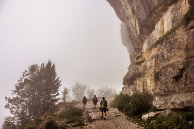 Hikers walking on road by rocky mountain during foggy weather