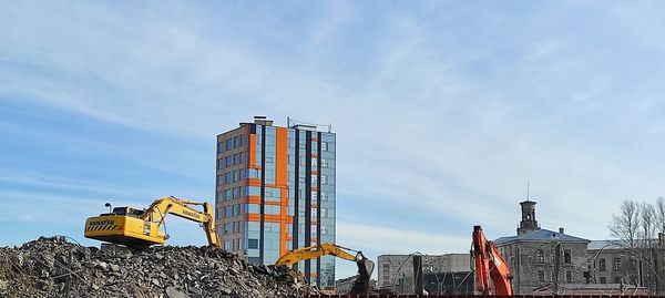 Low angle view of crane by building against sky