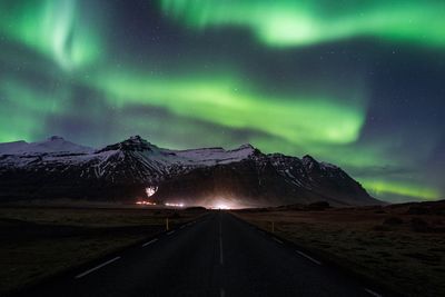 Road leading towards mountain during aurora borealis