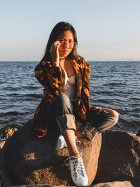 Young woman sitting on sea shore against sky