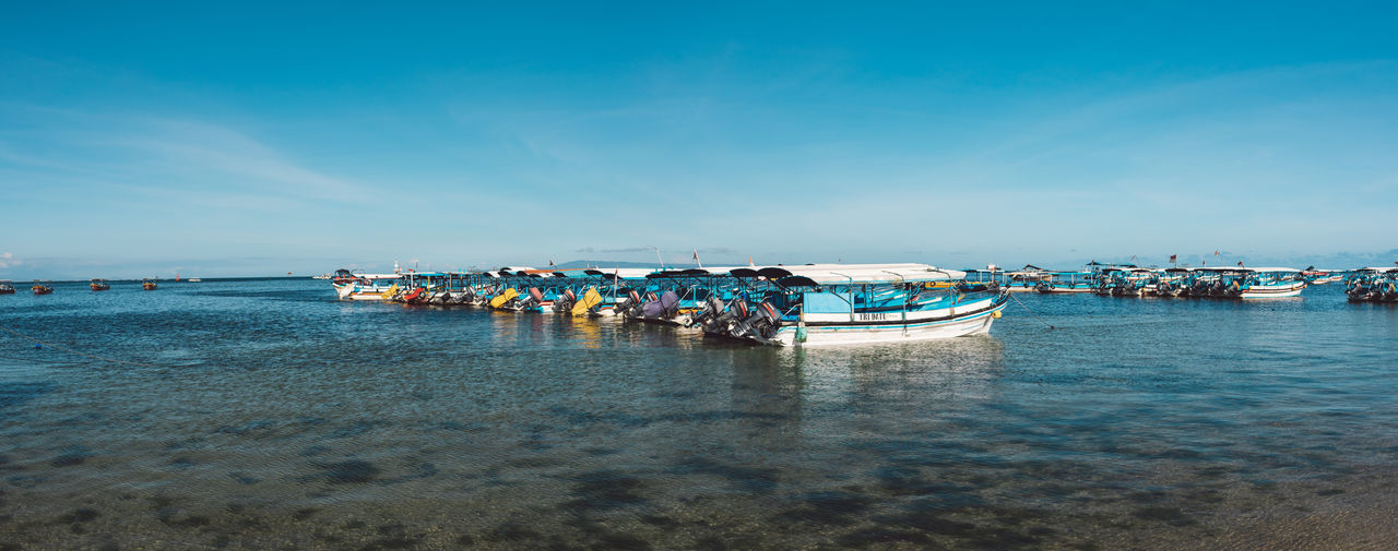 BOATS MOORED IN SEA AGAINST BLUE SKY