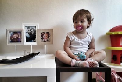 Cute girl sucking pacifier while sitting on table at home