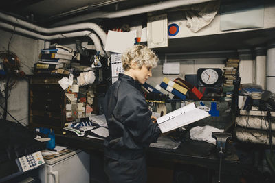 Side view of female mechanic reading document while standing in auto repair shop