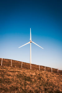 Low angle view of windmill on field against clear blue sky