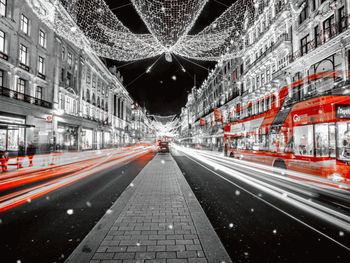 Digital composite image of light trails on road amidst buildings in city