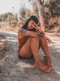 Portrait of woman showing peace sign while sitting on road