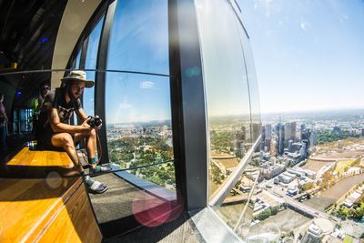 Woman sitting in city against sky