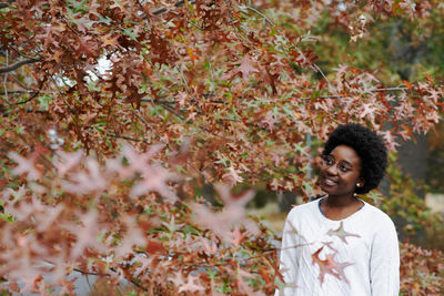 Young woman looking away while standing by tree