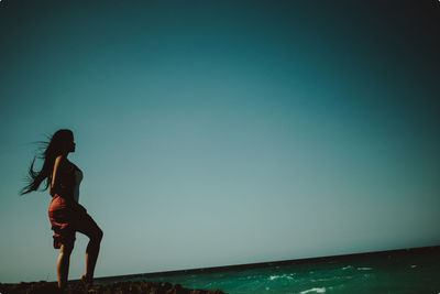 Side view of woman standing by sea against clear sky