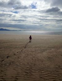 Man standing on beach against cloudy sky