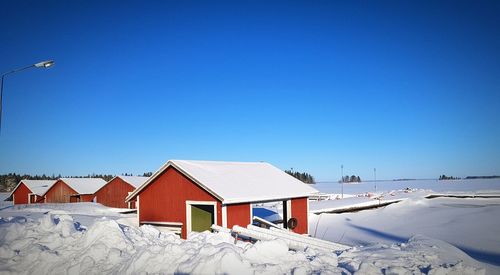 House on snow covered land against clear blue sky