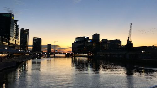 River by illuminated buildings against sky during sunset