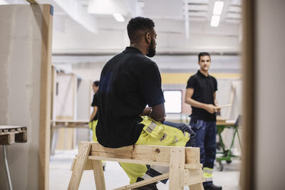 Rear view of carpentry student sitting on wooden structure at workshop