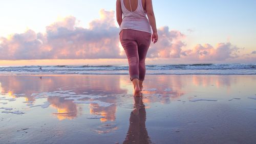 Rear view of woman standing at beach during sunset