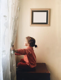 Side view of girl standing against wall at home
