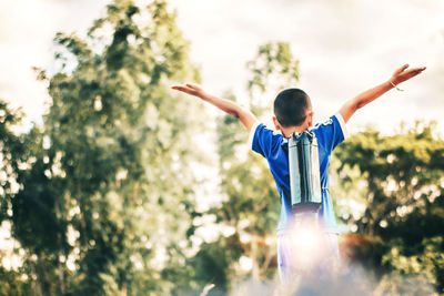 Rear view of boy with arms outstretched against trees