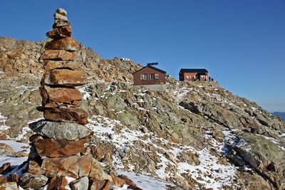 Stack of rocks by houses on mountain against clear blue sky during winter
