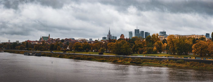 Buildings by river against cloudy sky