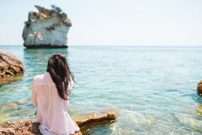 Rear view of woman on rock by sea against sky