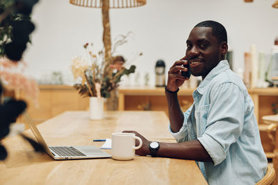 Young man using mobile phone while sitting on table