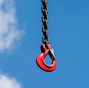 Low angle view of hook hanging from chain against sky during sunny day