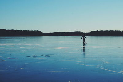 Man ice-skating on frozen lake against sky