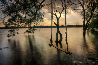 Silhouette tree by lake against sky during sunset