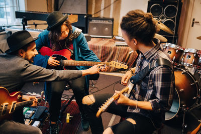 Man teaching female friend while playing guitar at recording studio during rehearsals