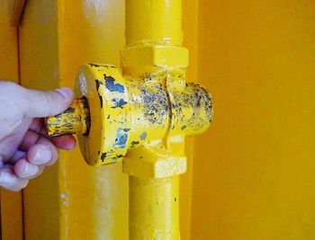 Close-up of human hand holding metal against yellow wall
