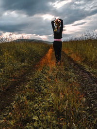Rear view of woman with hand in hair standing on land against sky during sunset